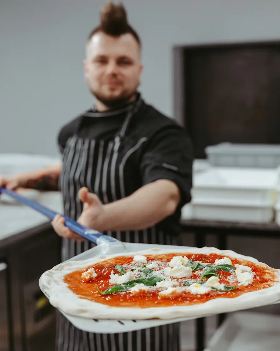 Pizzaiolo holding a peel with a freshly baked pizza