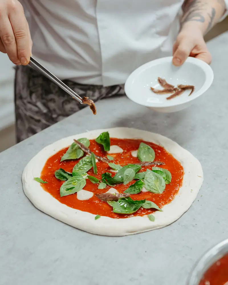 Pizzaiolo’s hands placing basil on a pizza before baking